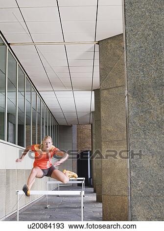 Woman jumping hurdles outside building View Large Photo Image Stock Image - Woman jumping hurdles outside building. Fotosearch