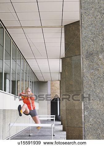 Woman jumping hurdles outside building View Large Photo Image Stock Photo - Woman jumping hurdles outside building. Fotosearch