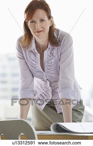 Stock Image - Woman leaning on desk in office portrait. Fotosearch