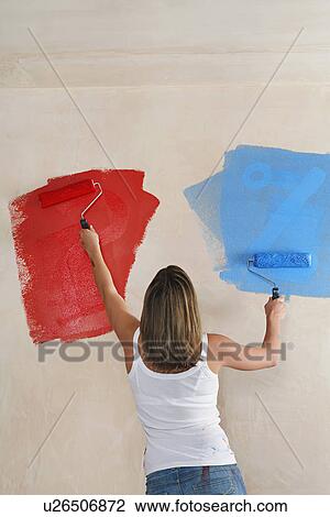 Stock Image - Woman painting wall with paint rollers back view. Fotosearch