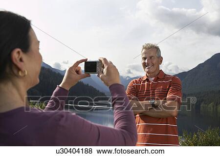 Stock Photo - Woman photographing man mountains in background. Fotosearch