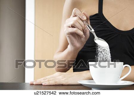Stock Image - Woman pouring sugar into tea cup mid section close up. Fotosearch