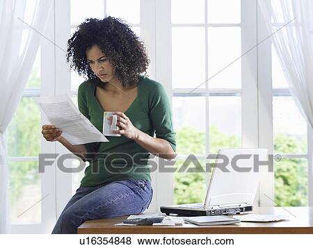 Woman reading paper document sitting on desk View Large Photo Image Stock Photo - Woman reading paper document sitting on desk. Fotosearch