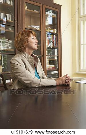 Stock Photo - Woman sitting at table in living room. Fotosearch
