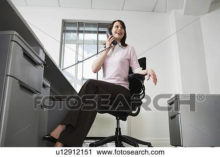 Woman sitting behind desk in office using phone and smiling low angle view View Large Photo Image Stock Image - Woman sitting behind desk in office using phone and smiling low angle view. Fotosearch