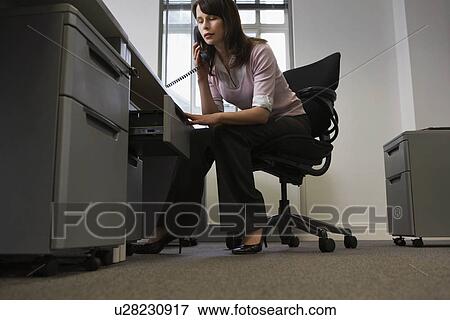 Woman sitting behind desk in office using phone and opening drawer View Large Photo Image Stock Photo - Woman sitting behind desk in office using phone and opening drawer. Fotosearch