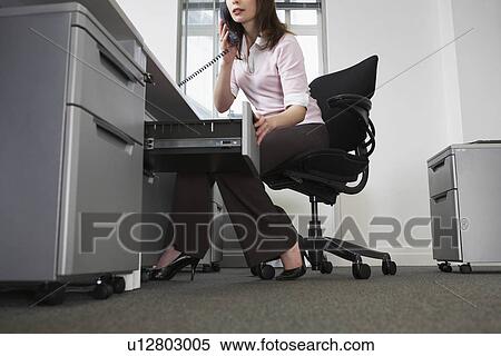 Woman sitting behind desk in office using phone and opening drawer View Large Photo Image Stock Photography - Woman sitting behind desk in office using phone and opening drawer. Fotosearch