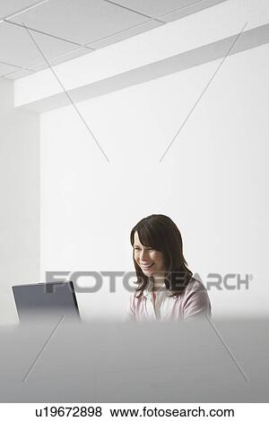 Woman sitting in office using laptop and smiling View Large Photo Image Stock Photo - Woman sitting in office using laptop and smiling. Fotosearch