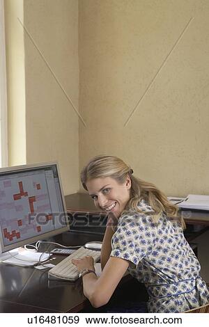 Stock Photo - Woman smiling by computer in office. Fotosearch
