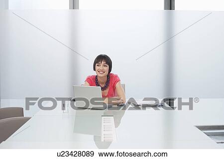 Woman smiling by laptop in modern cubicle View Large Photo Image Stock Photo - Woman smiling by laptop in modern cubicle. Fotosearch