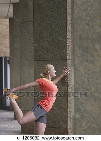 Stock Image - Woman stretching against a pillar. Fotosearch
