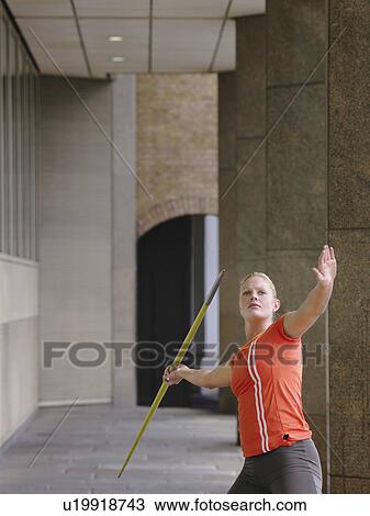 Stock Image - Woman throwing javelin outside building. Fotosearch