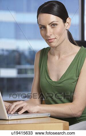 Woman using laptop at desk in office portrait View Large Photo Image Stock Image - Woman using laptop at desk in office portrait. Fotosearch