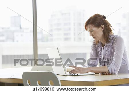 Stock Photograph - Woman using laptop at desk in office. Fotosearch