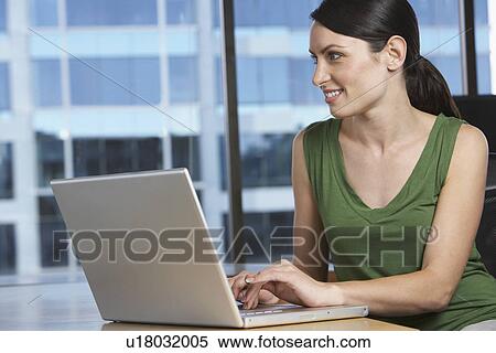 Stock Photography - Woman using laptop at desk in office. Fotosearch