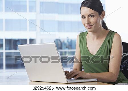 Stock Photography - Woman using laptop at desk in office portrait. Fotosearch