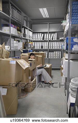 Stock Photo - Woman using laptop between boxes in storage room. Fotosearch
