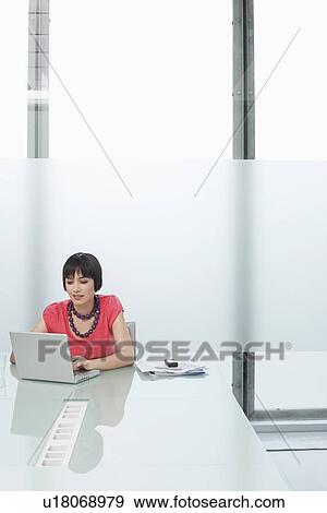 Stock Photo - Woman using laptop in modern cubicle. Fotosearch