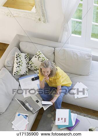 Stock Image - Woman using laptop sitting on sofa elevated view. Fotosearch