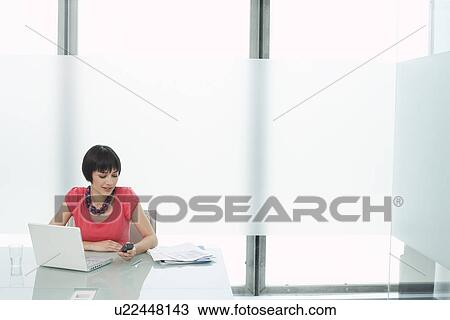 Woman using mobile phone and laptop in modern cubicle View Large Photo Image Stock Image - Woman using mobile phone and laptop in modern cubicle. Fotosearch
