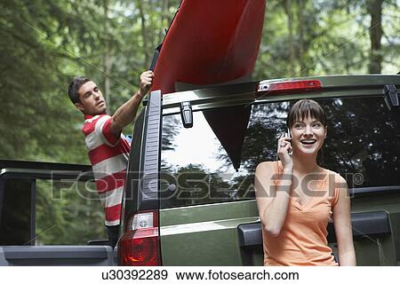 Woman using mobile phone by car man tying kayak on roof in forest View Large Photo Image Stock Photo - Woman using mobile phone by car man tying kayak on roof in forest. Fotosearch