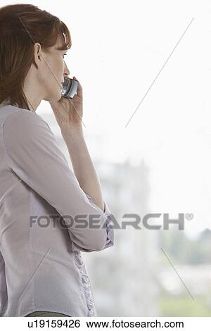 Stock Photograph - Woman using mobile phone by window. Fotosearch