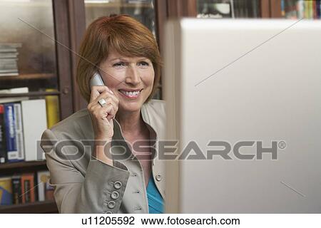 Woman using mobile phone while on computer in living room View Large Photo Image Stock Image - Woman using mobile phone while on computer in living room. Fotosearch