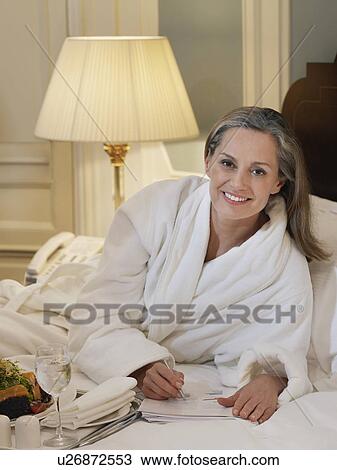 Stock Image - Woman wearing bathrobe writing lying on bed portrait. Fotosearch