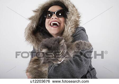 Stock Photograph - Woman wearing hooded coat holding cat laughing. Fotosearch