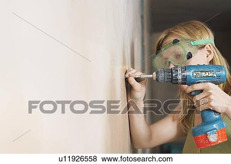 Woman wearing protective goggles drilling wall close-up View Large Photo Image Stock Photo - Woman wearing protective goggles drilling wall close-up. Fotosearch