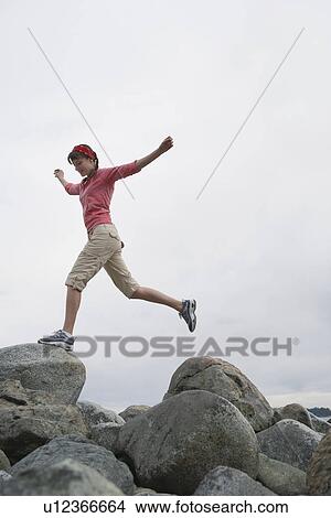 Woman with arms outstretched jumping on rocks View Large Photo Image Picture - Woman with arms outstretched jumping on rocks. Fotosearch