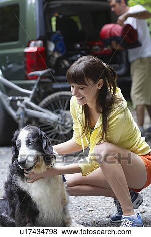 Stock Photo - Woman with dog outdoors man loading car in background. Fotosearch
