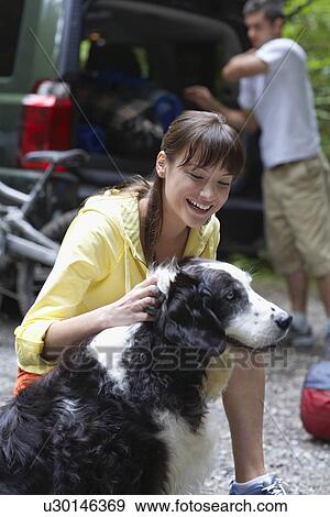 Woman with dog outdoors man loading car in background View Large Photo Image Stock Photo - Woman with dog outdoors man loading car in background. Fotosearch