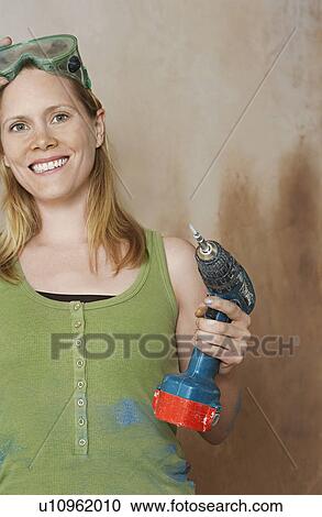Stock Image - Woman with protective goggles holding power drill portrait. Fotosearch