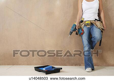 Woman with toolbelt and drill leaning against wall low section View Large Photo Image Stock Image - Woman with toolbelt and drill leaning against wall low section. Fotosearch