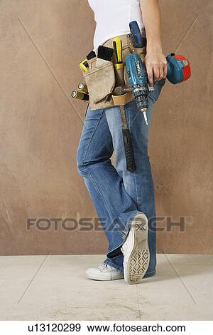 Stock Photo - Woman with toolbelt and drill leaning against wall low section. Fotosearch