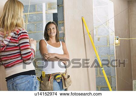 Woman with toolbelt leaning against wall taling to friend View Large Photo Image Picture - Woman with toolbelt leaning against wall taling to friend. Fotosearch