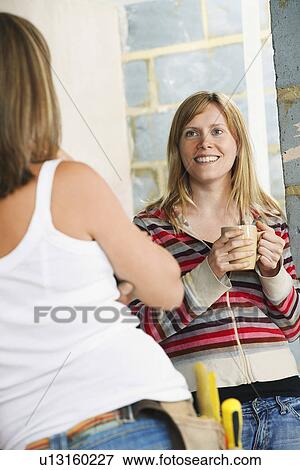Woman with toolbelt leaning against wall talking to friend View Large Photo Image Stock Photo - Woman with toolbelt leaning against wall talking to friend. Fotosearch