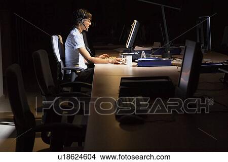 Picture - Woman working at laptop in dark office. Fotosearch