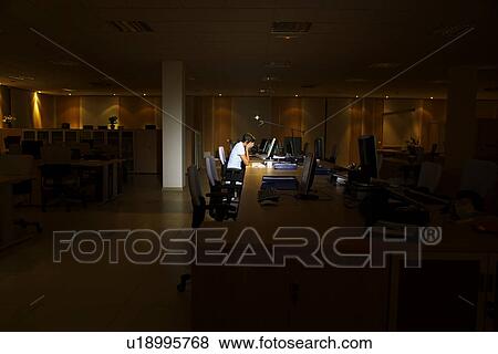 Stock Photo - Woman working at laptop in dark office. Fotosearch