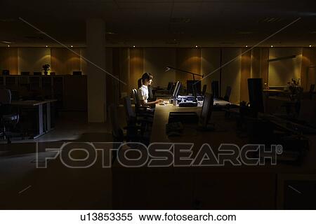 Stock Photography - Woman working at laptop in dark office. Fotosearch