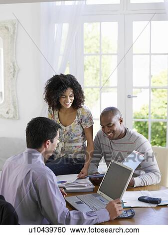 Stock Image - Young African American couple discussing home finances with financial advisor at dining room table. Fotosearch