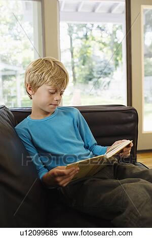 Young boy (5-6) sitting on sofa reading book View Large Photo Image Stock Photography - Young boy (5-6) sitting on sofa reading book. Fotosearch