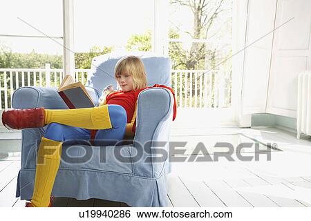 Young boy (7-9) sitting in armchair reading wearing superhero costume View Large Photo Image Stock Photograph - Young boy (7-9) sitting in armchair reading wearing superhero costume. Fotosearch