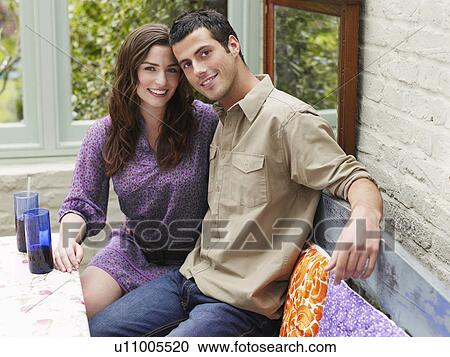 Stock Image - Young couple sitting at verandah table smiling portrait. Fotosearch