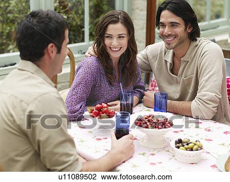 Young couple sitting at verandah table smiling to friend elevated view View Large Photo Image Stock Image - Young couple sitting at verandah table smiling to friend elevated view. Fotosearch