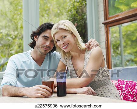 Stock Photograph - Young couple sitting at verandah table smiling portrait. Fotosearch