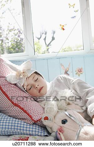 Young girl (5-6) in unicorn costume sleeping on bed with toy horse View Large Photo Image Stock Photo - Young girl (5-6) in unicorn costume sleeping on bed with toy horse. Fotosearch