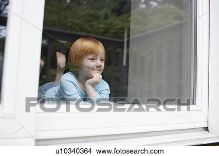 Picture - Young girl (5-6) indoors looking through window. Fotosearch
