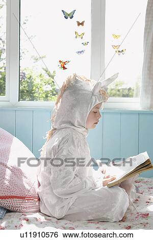 Young girl (5-6) sitting on bed in unicorn costume reading book side view View Large Photo Image Stock Photograph - Young girl (5-6) sitting on bed in unicorn costume reading book side view. Fotosearch